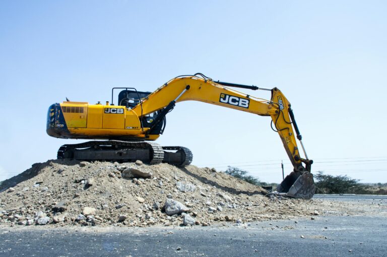 Yellow excavator on a pile of dirt at a construction site under clear blue sky.